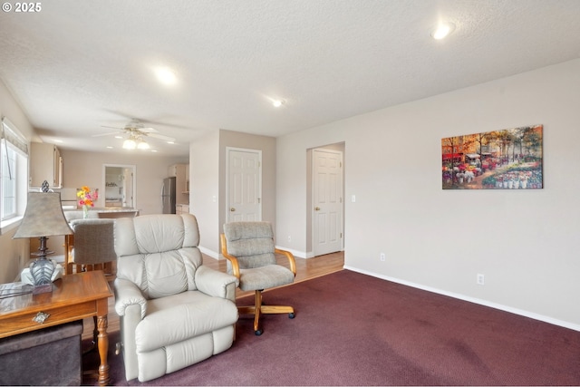 living area featuring a textured ceiling, carpet, a ceiling fan, and baseboards