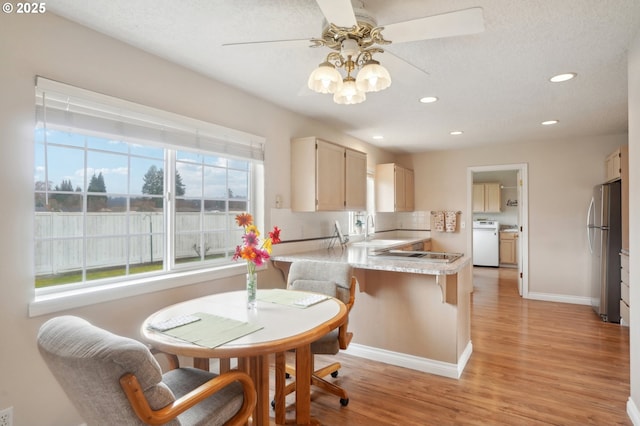 kitchen featuring light wood finished floors, light countertops, freestanding refrigerator, a sink, and a peninsula