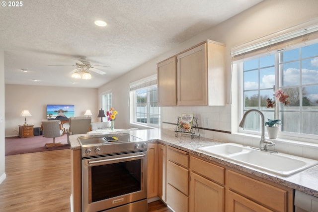 kitchen featuring a peninsula, a sink, light wood-style floors, open floor plan, and stainless steel range with electric stovetop