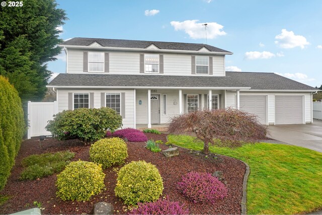 traditional-style house featuring a porch, a shingled roof, concrete driveway, an attached garage, and fence