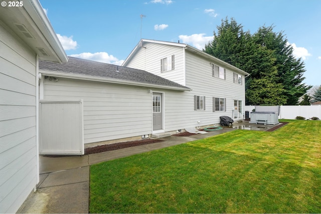 back of house featuring roof with shingles, a patio, a lawn, a hot tub, and fence