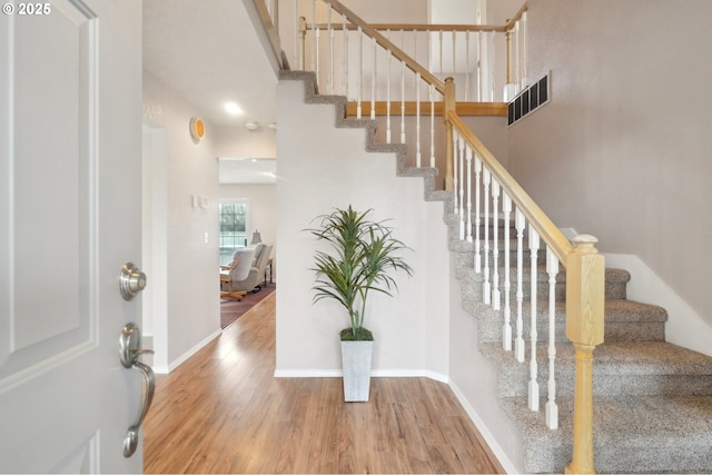 stairs with visible vents, a towering ceiling, baseboards, and wood finished floors