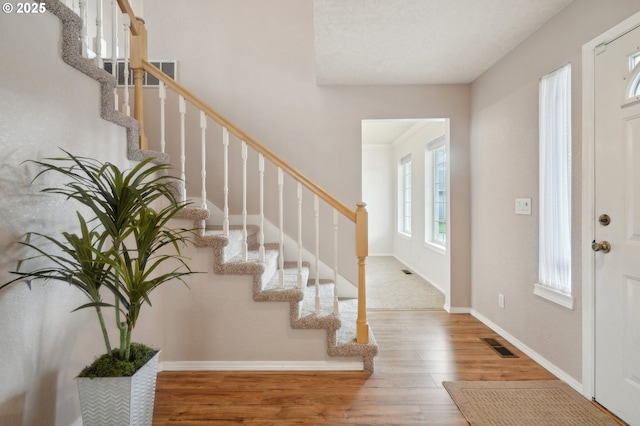 foyer with stairs, visible vents, baseboards, and wood finished floors