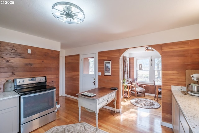 kitchen with wood walls, stainless steel electric range, light stone countertops, and light hardwood / wood-style flooring