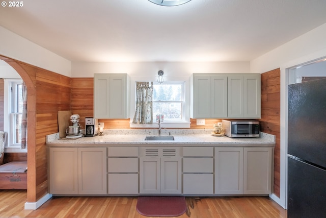 kitchen featuring sink, black fridge, light hardwood / wood-style floors, gray cabinets, and wooden walls