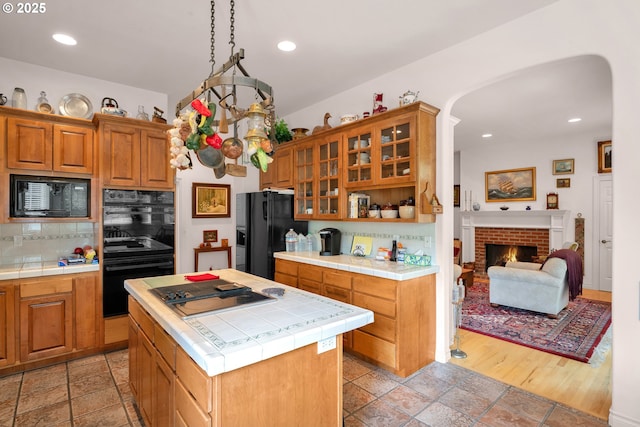 83485 Clear Lake Rd, Florence, OR 97439 - kitchen with black appliances, tile countertops, arched walkways, tasteful backsplash, and glass insert cabinets