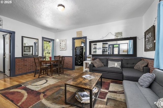 living room with hardwood / wood-style flooring, a textured ceiling, and brick wall