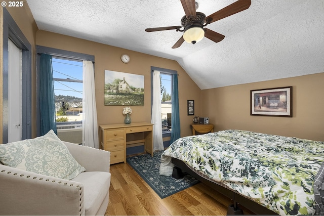 bedroom with ceiling fan, light hardwood / wood-style floors, vaulted ceiling, and a textured ceiling