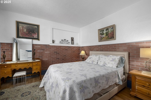 bedroom with brick wall, dark hardwood / wood-style flooring, and a textured ceiling