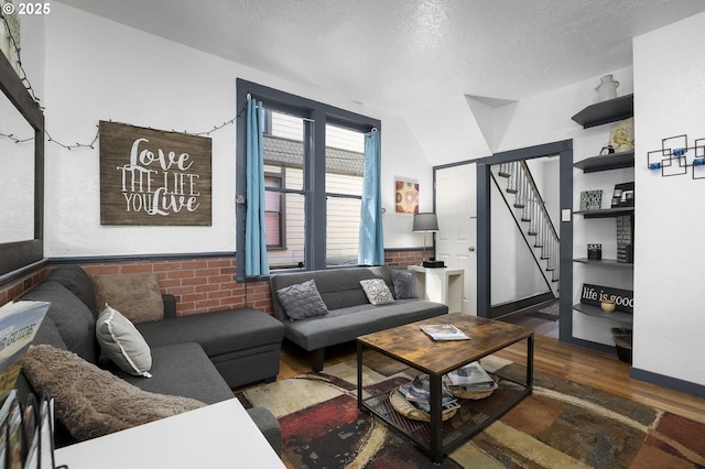 living room featuring vaulted ceiling, brick wall, dark wood-type flooring, and a textured ceiling