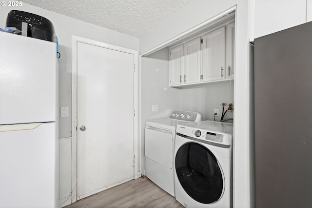 4973 Wagon Trail Ct, Salem, OR 97317 - laundry area featuring washing machine and dryer, light wood-style flooring, cabinet space, and a textured ceiling