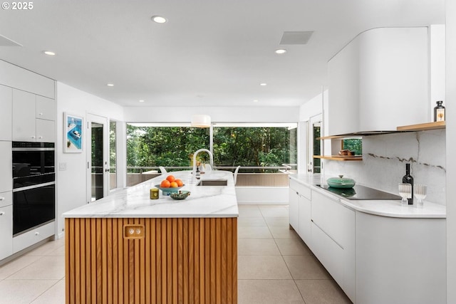 kitchen featuring white cabinets, a kitchen island with sink, decorative backsplash, and sink