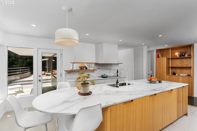 kitchen with decorative light fixtures, a kitchen island with sink, light tile patterned flooring, light stone countertops, and sink