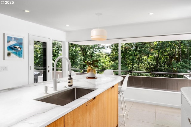 kitchen featuring light stone countertops, light tile patterned floors, pendant lighting, and sink