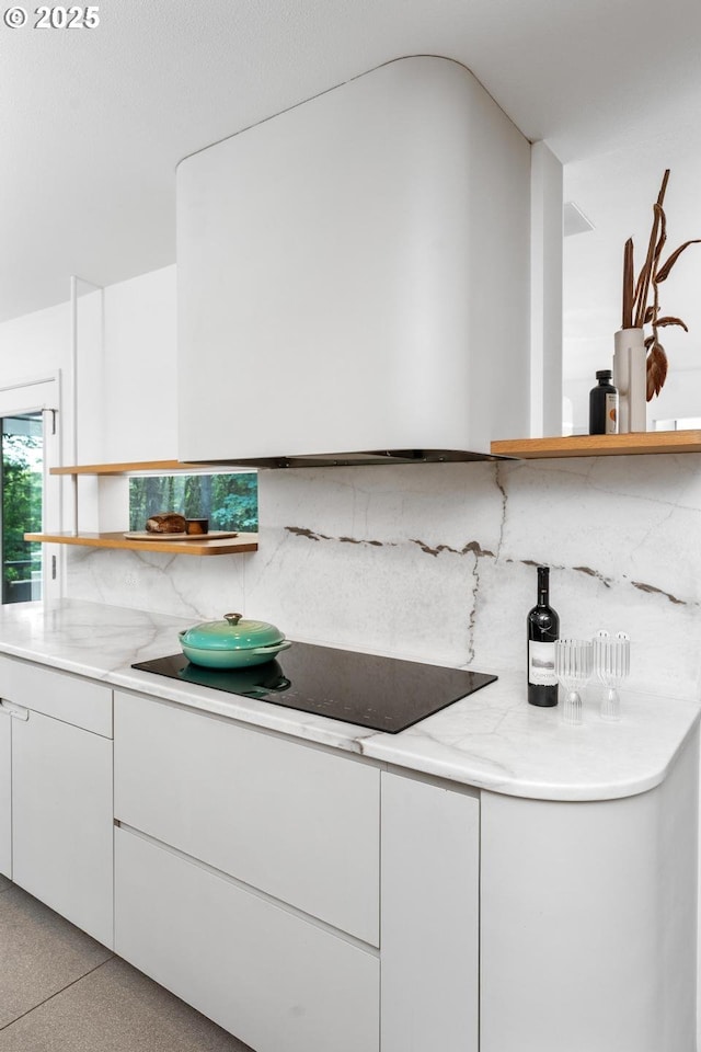 kitchen featuring tasteful backsplash, white cabinets, light stone countertops, and black electric stovetop