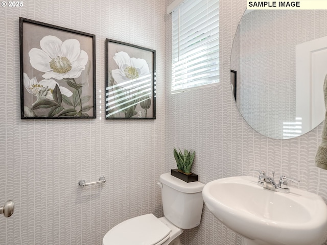 bathroom featuring wallpapered walls, toilet, and a sink