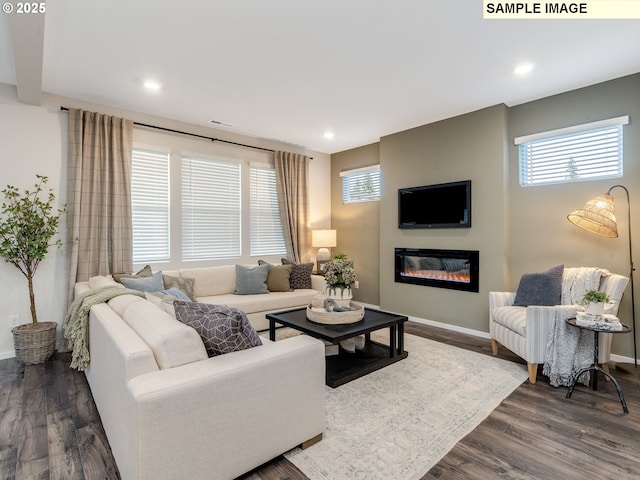 living area with a glass covered fireplace, plenty of natural light, dark wood-type flooring, and baseboards