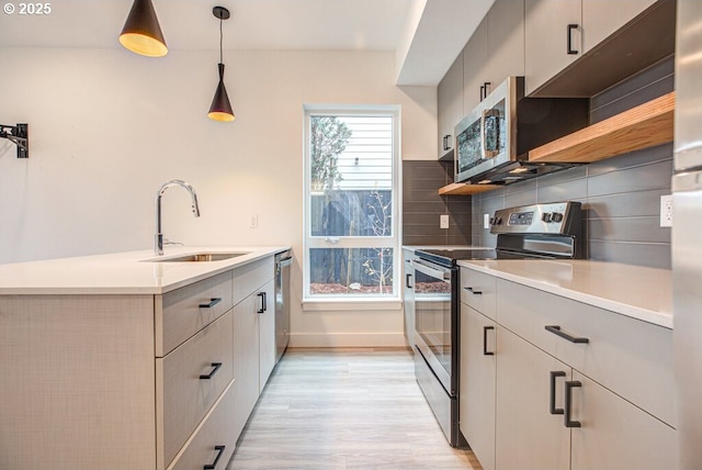 kitchen featuring sink, hanging light fixtures, stainless steel appliances, backsplash, and light hardwood / wood-style floors