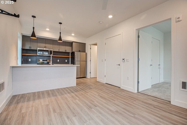 kitchen featuring backsplash, light hardwood / wood-style flooring, appliances with stainless steel finishes, decorative light fixtures, and kitchen peninsula