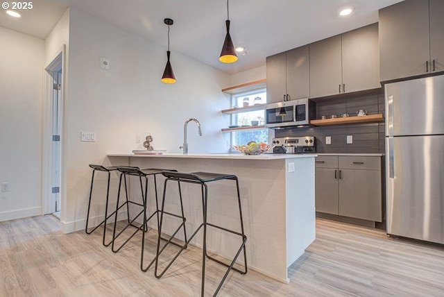 kitchen featuring kitchen peninsula, appliances with stainless steel finishes, a kitchen bar, and gray cabinetry