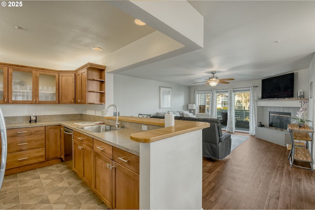 kitchen with brown cabinetry, a peninsula, a sink, a tiled fireplace, and open floor plan