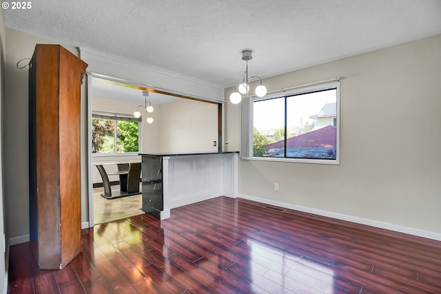 unfurnished dining area with a textured ceiling, a chandelier, baseboards, wood finished floors, and visible vents