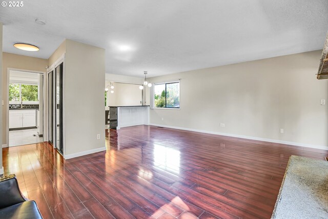 unfurnished living room with baseboards, wood finished floors, and a chandelier