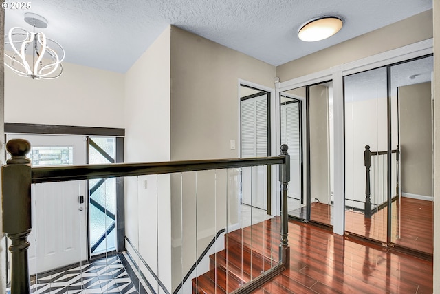 corridor with an inviting chandelier, a textured ceiling, wood finished floors, and an upstairs landing