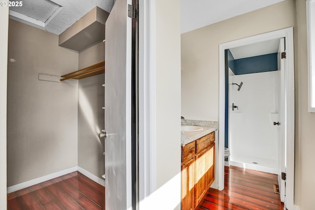 full bathroom featuring a shower, wood finished floors, vanity, baseboards, and toilet