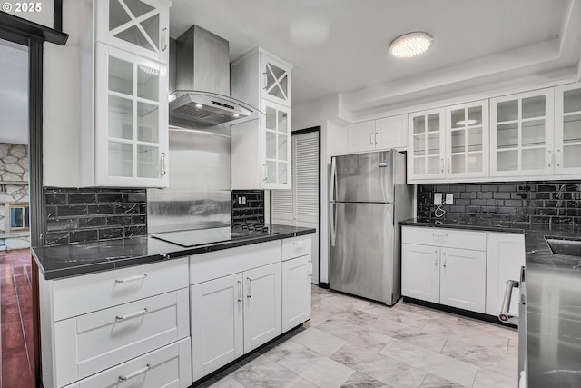 kitchen with wall chimney range hood, glass insert cabinets, freestanding refrigerator, and backsplash