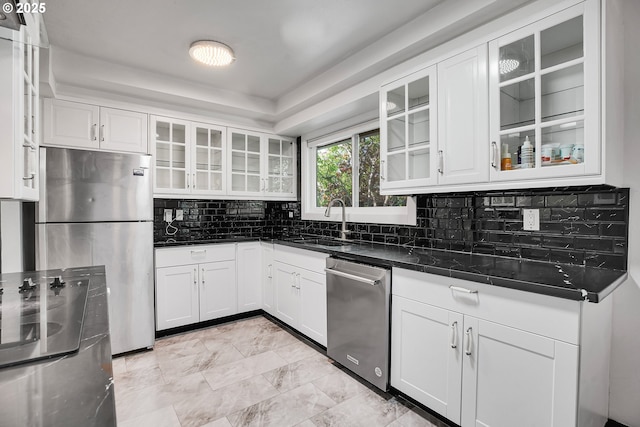 kitchen featuring dark countertops, a sink, white cabinets, glass insert cabinets, and stainless steel appliances