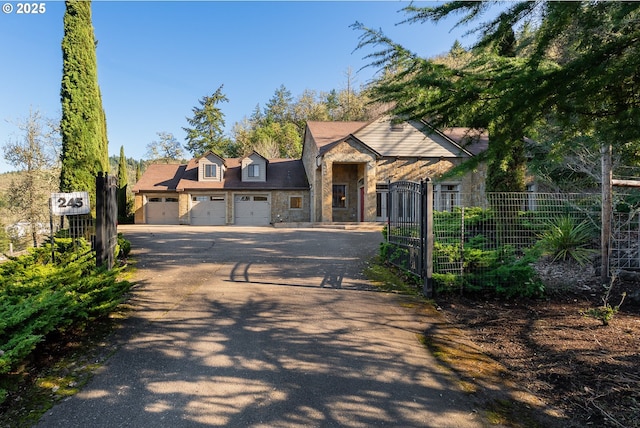 view of front of house with an attached garage, fence, driveway, stone siding, and a gate