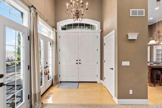 entryway featuring a high ceiling, light wood-style flooring, a chandelier, french doors, and baseboards