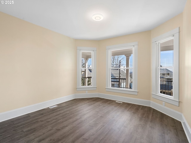 empty room featuring dark wood-type flooring, visible vents, and baseboards