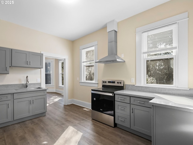 kitchen with gray cabinets, stainless steel range with electric cooktop, a sink, and wall chimney exhaust hood