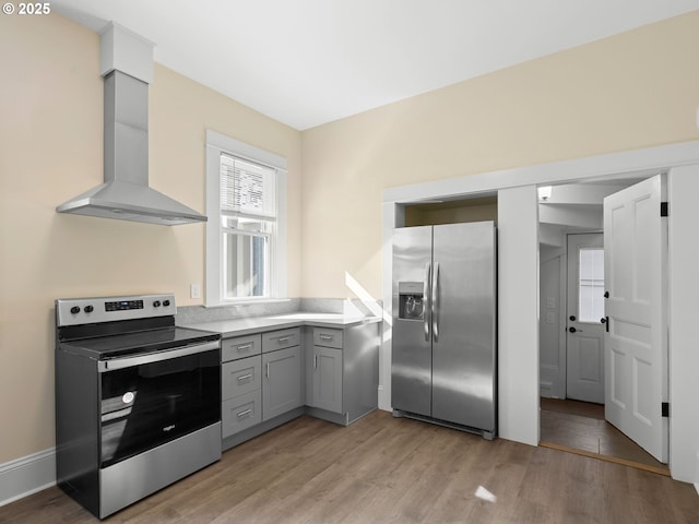 kitchen featuring stainless steel appliances, light wood finished floors, wall chimney exhaust hood, and gray cabinets