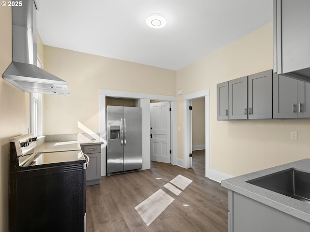 kitchen with stainless steel fridge with ice dispenser, wood finished floors, gray cabinets, wall chimney range hood, and black range with electric cooktop