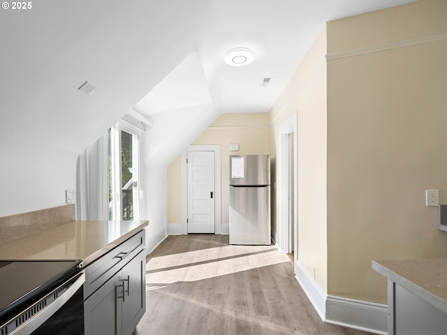 kitchen featuring lofted ceiling, visible vents, baseboards, freestanding refrigerator, and light wood finished floors