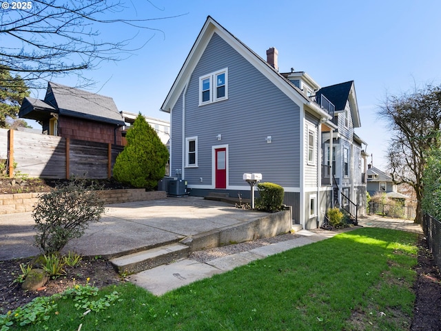 rear view of property with entry steps, central AC, fence, a lawn, and a chimney