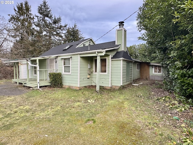 rear view of property featuring a deck, a shingled roof, a lawn, and a chimney