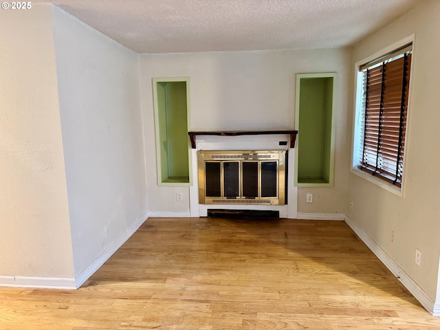 unfurnished living room featuring a glass covered fireplace, a textured ceiling, baseboards, and wood finished floors