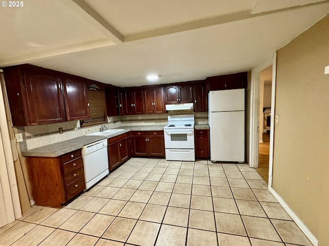 kitchen with white appliances, light tile patterned floors, beamed ceiling, under cabinet range hood, and a sink