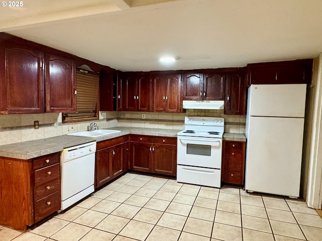 kitchen with light tile patterned floors, under cabinet range hood, white appliances, a sink, and backsplash