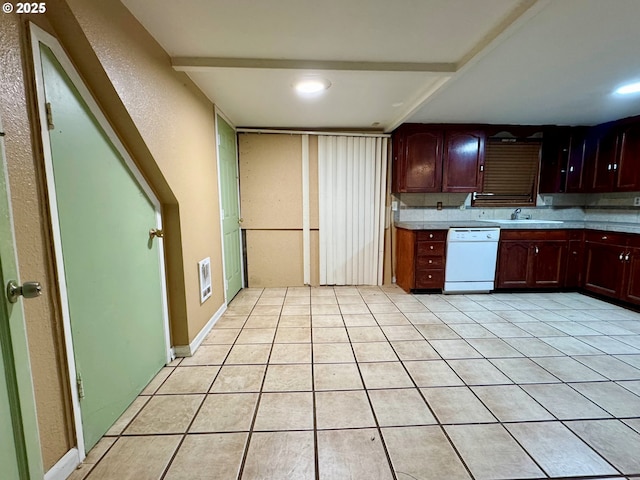 kitchen featuring light countertops, a textured wall, light tile patterned flooring, a sink, and dishwasher