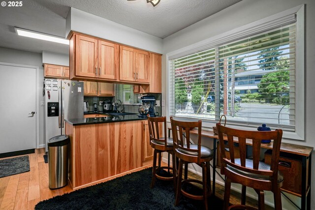 7360 SE Imperial Ct, Milwaukie, OR 97222 - kitchen featuring stainless steel fridge, dark countertops, a peninsula, wood finished floors, and tasteful backsplash