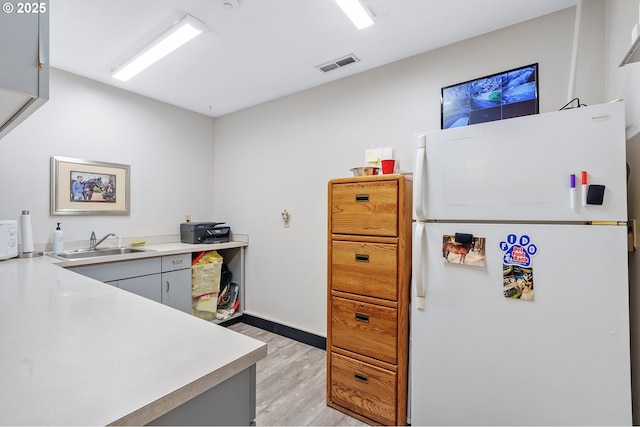 kitchen with white refrigerator, light hardwood / wood-style floors, sink, and gray cabinetry