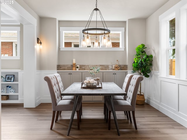 dining room featuring light wood-style floors, a decorative wall, and a wainscoted wall