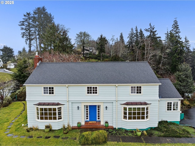 view of front facade featuring a front yard, roof with shingles, and a chimney