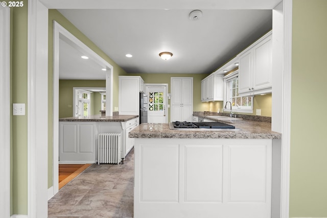 kitchen featuring stainless steel gas stovetop, radiator heating unit, white cabinetry, a sink, and a peninsula