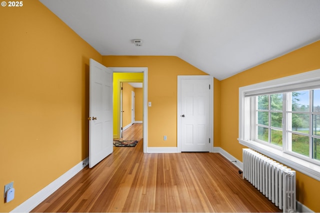 unfurnished bedroom with vaulted ceiling, light wood finished floors, radiator heating unit, and baseboards